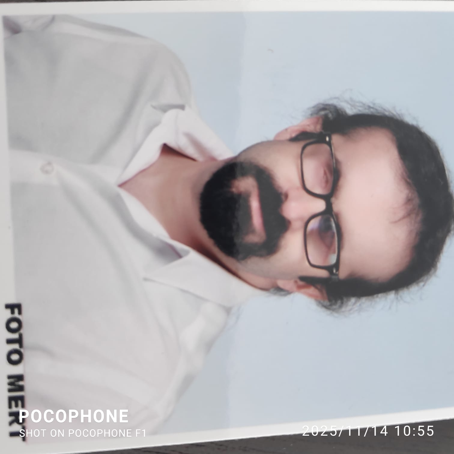 Beyaz gömlek giymiş ve gözlük takmış Süleyman YİĞİT’in, sade, açık renkli bir arka plan önünde yakından çekilmiş görüntüsü.